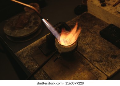 Melting gold in a small crucible for making jewelry. Goldsmith using torch flame to heat and melt the silver granules in a crucible.
