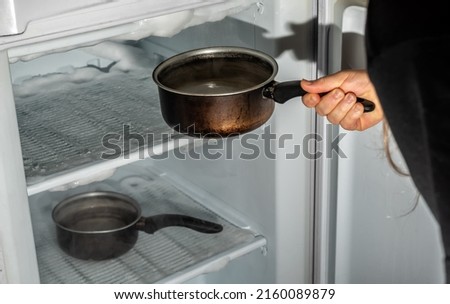 Melting the ice from the freezer with the help of saucepans with hot water. Stock photo © 