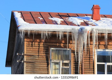 Melting Snow And Icicles Hanging On The Roof Of A Wooden House Against Blue Sky In Early Spring