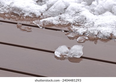 Melting snow on the surface of exotic wood outdoor balcony, thaw during winter, end of frosty weather.