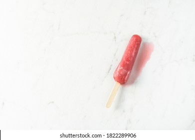 Melting Strawberry Popsicle With A Puddle Next To It In Summer On A White Marble Table With Copy Space; Color