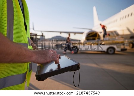 Member of ground crew preparing airplane before flight. Worker using tablet against plane at airport.

