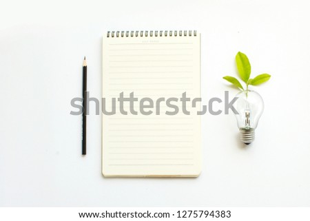Memo pad and light bulb icon with growing plant on white table top. Conceptual brainstorming image.