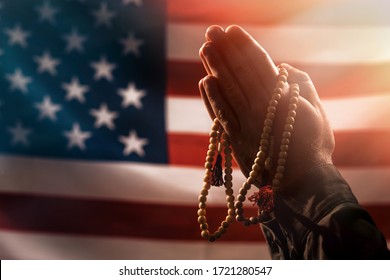 Memorial day, veterans day. Male hands folded in prayer, holding a rosary. The American flag is in the background. The concept amerikanskih holidays and religion - Powered by Shutterstock