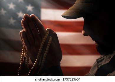 Memorial day, veterans day. A soldier holds a rosary in his hands and prays holding it to his face. Close up. American flag on the background. Concept of American holidays and religion - Powered by Shutterstock