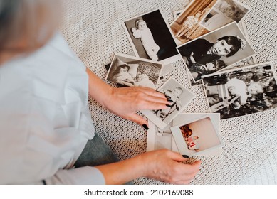 Memories of childhood, nostalgia of youth concept. Close-up of caucasian woman looking at her baby vintage photo while sitting on sofa, indoors. Selective focus on monochrome retro pictures, top view - Shutterstock ID 2102169088