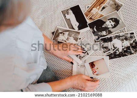 Memories of childhood, nostalgia of youth concept. Close-up of caucasian woman looking at her baby vintage photo while sitting on sofa, indoors. Selective focus on monochrome retro pictures, top view
