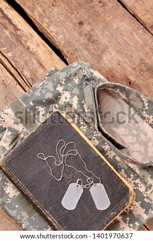 In memory of a brave soldier. Military camouflage clothes, old book, and dog tags on wood.