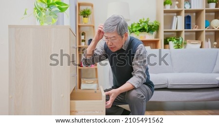 memory error concept - asian older man wearing reading glasses is rummaged in all drawers while looking for something that he forgot it