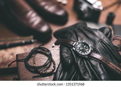 Men accessories on wooden desk. Closeup at luxury men watch with black dial and leather strap.