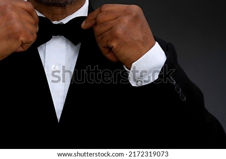 men adjusting his bow tie on grey background with people stock photo 