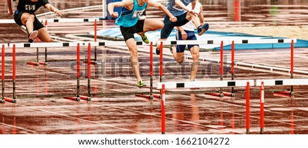 men athletes run 110 meters hurdles in athletics in rainy weather