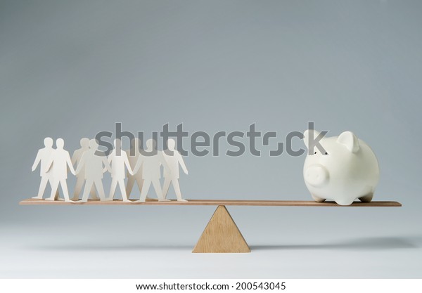 Men balanced on\
seesaw over a piggy bank