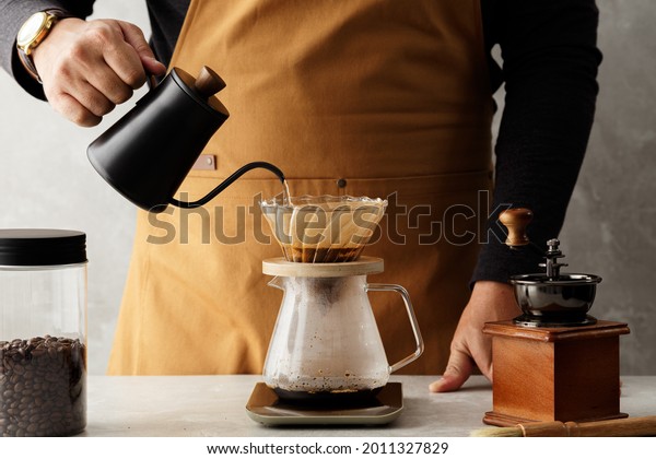 Men barista making a drip coffee,
pouring hot water from kettle over a ground coffee
powder