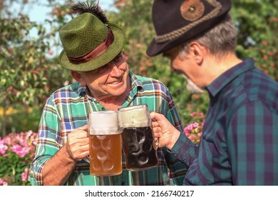 Men with beer mugs with Bavarian beer in Tyrolean hats with feathers celebrating beer festival outdoor among the trees in Germany. Happy old Germans people. October Munich holiday on sunny day.