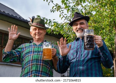 Men with beer mugs with Bavarian beer in Tyrolean hats with feathers celebrating beer festival outdoor among the trees in Germany. Happy old Germans people. October Munich holiday on sunny day.
