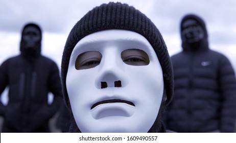 Men In Black Jackets And Masks. Footage. Criminal Gang In Black Plastic Masks And Leader In White Mask On Background Of Cloudy Sky. Masked Social Criminal Gang