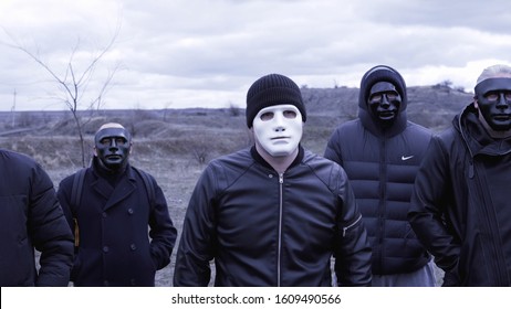 Men in black jackets and masks. Footage. Criminal gang in black plastic masks and leader in white mask on background of cloudy sky. Masked social criminal gang