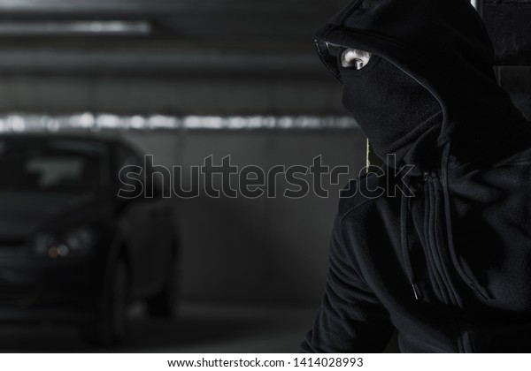 Men in Black Mask is\
About to Steal Modern Car on a Parking Lot. Illegal Activity\
Conceptual Photo.