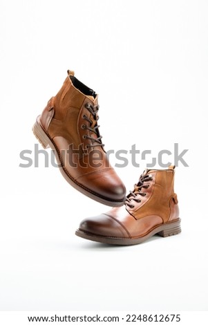 Men boots casual style in brown colour over a white background. Side view, one foot flying  in the air. Copy space for ad, design, text.