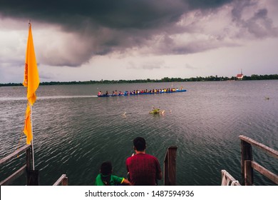 Men And Children Are Sitting And Watching A Long Rowing Boat Ride On The River In Sakon Nakhon Province, Thailand.-25 August 2019