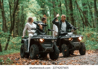 Men doing high five. Two couples on a quad bike in the forest during the day.