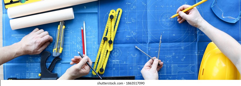 Men draftsmans on table draw construction project. An architect builds project on paper using measuring instruments. Builders calculate risks building. Joint work design department and builder