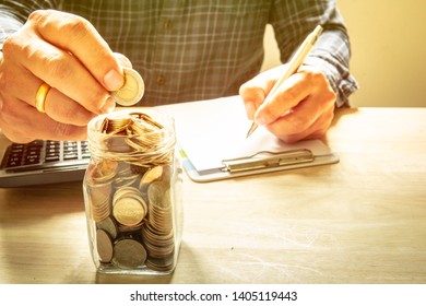 Men Are Dropping Money To Glass Jars And Writing Notes. And Have A Calculator Placed On A Wooden Table Offering Savings And Calculating Money To Spend. Success Concept. - Image