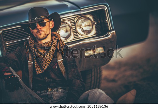 The\
Men of the Far West. Caucasian Western Wear Men in His 30s Relaxing\
in Front of His Classic Muscle Car. American\
West.