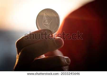 Men Hand hold ethereum silver Coin with the acronym ETH. Ethereum is one of the main cryptocurrencies and assest on blockchain exchanges which investors choose to protect their savings. Ethereum logo