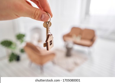 Men hand holding key with house shaped keychain. Modern light lobby interior. Mortgage concept. Real estate, moving home or renting property. - Shutterstock ID 1705080001