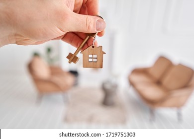 Men Hand Holding Key With House Shaped Keychain. Modern Light Lobby Interior. Mortgage Concept. Real Estate, Moving Home Or Renting Property.