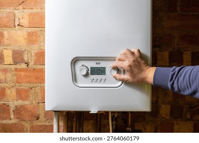 Men hand setting temperature button on control panel of central heating at combi boiler. Incressing price for gas