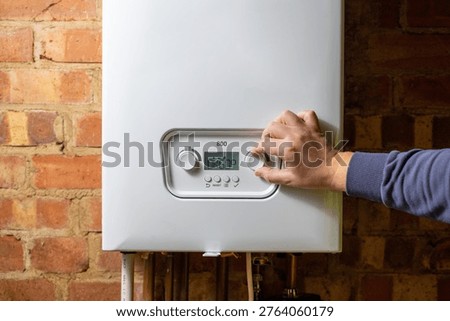 Men hand setting temperature button on control panel of central heating at combi boiler. Incressing price for gas