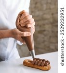 Men hands of a confectioner squeeze chocolate cream from a pastry bag through a shaped nozzle, vertical view 