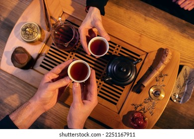 Men hands holding cups with chinese tea. View from above at the wooden table with traditional chinese tea ceremony accesories and cups of tea. Couple people  - Powered by Shutterstock