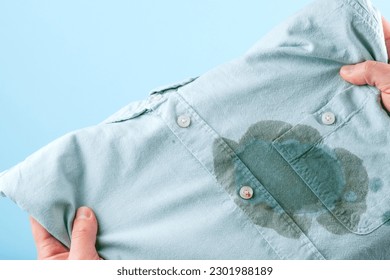 Men hands showing a dirty shirt and visual evaluation of stain on clothes on a blue background. Spoiled linen. isolated. High quality photo