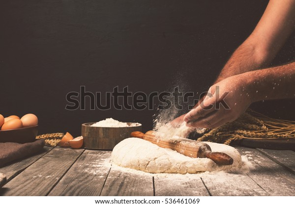 Men hands sprinkle a dough with flour close up. Man\
preparing bread dough