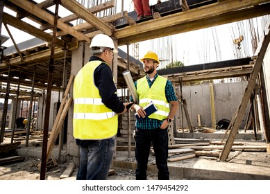 Men in hardhat and green jacket posing on building site.