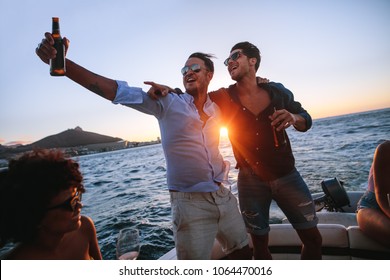Men having a great time at boat party at sunset. Friends partying on a yacht with drinks.
