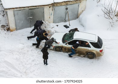 Men Help Push Out A Car Stuck In A Snowdrift On A Snowy Winter Day Near The Garage