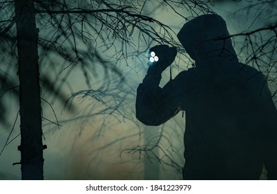 Men In His 40s With Flashlight Inside Dark Foggy Forest At Night. Performing Search During Night Hours. Missing People Theme.