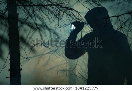 Men in his 40s with Flashlight Inside Dark Foggy Forest at Night. Performing Search During Night Hours. Missing People Theme.