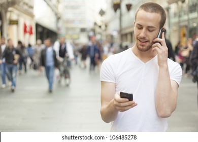 Men Holding In Hands Two Mobile Phone, City Street And People In Background