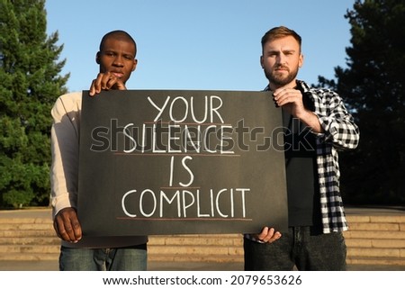 Men holding sign with phrase Your Silence Is Complicit outdoors. Racism concept