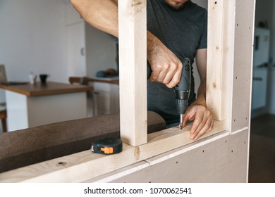 Men In Home Clothes Work With A Screwdriver, Fixing A Wooden Frame For A Window In Their House. Repair Yourself.