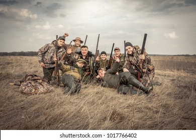 Men Hunters Group Team Portrait In Rural Field Posing Together Against Overcast Sky During Hunting Season. Concept For Teamwork.