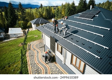 Men installers installing solar panel system on roof of house. Roofers in helmets lifting up photovoltaic solar module with help of ropes outdoors. Concept of alternative and renewable energy.