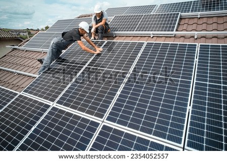 Men installers mounting photovoltaic solar moduls on roof of house. Engineers in helmets installing solar panel system outdoors. Concept of alternative and renewable energy. Aerial view.