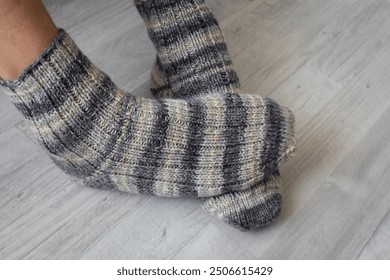 Men legs in knitted striped socks. Woolen knitted socks on crossed legs. Autumn warm clothing. Striped crochet pattern for socks. Handmade fashion. Cozy lifestyle. - Powered by Shutterstock